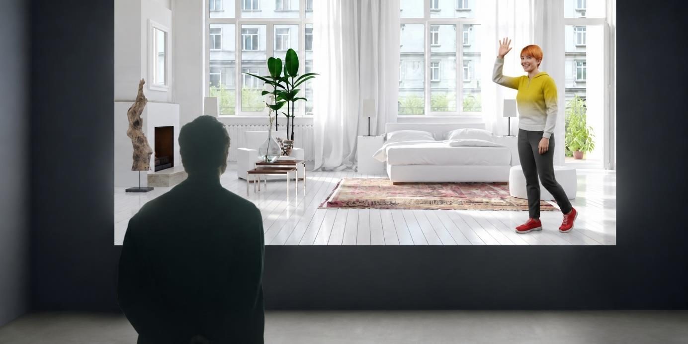 Een man, van achteren als silhouet, kijkt naar een groot scherm waarin een digitale vrouw in een gele trui zwaait in een lichte slaapkamer.