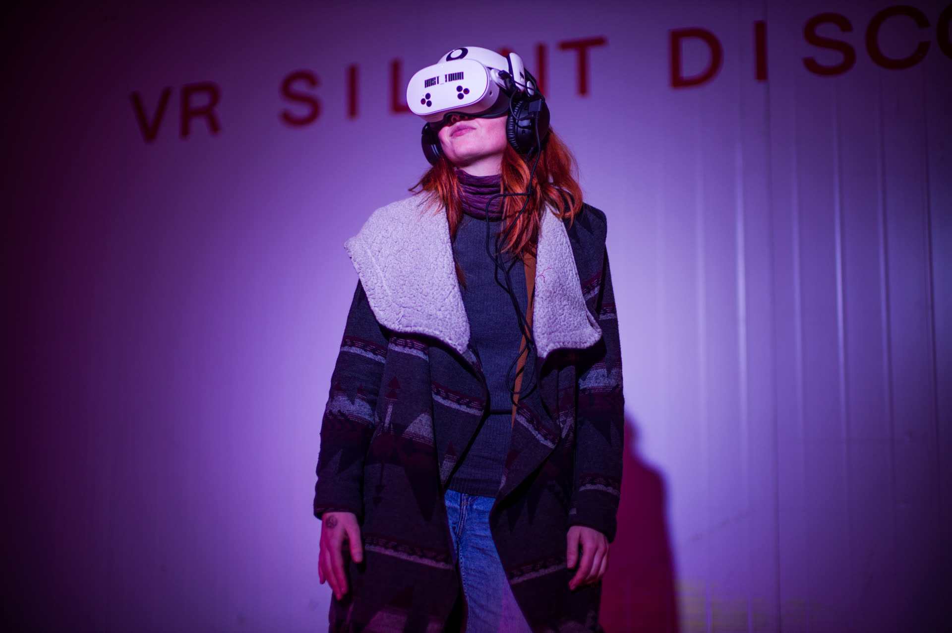 Een vrouw met rood haar, een witte VR-bril en een koptelefoon staat in paars licht voor de woorden VR Silent Disco.